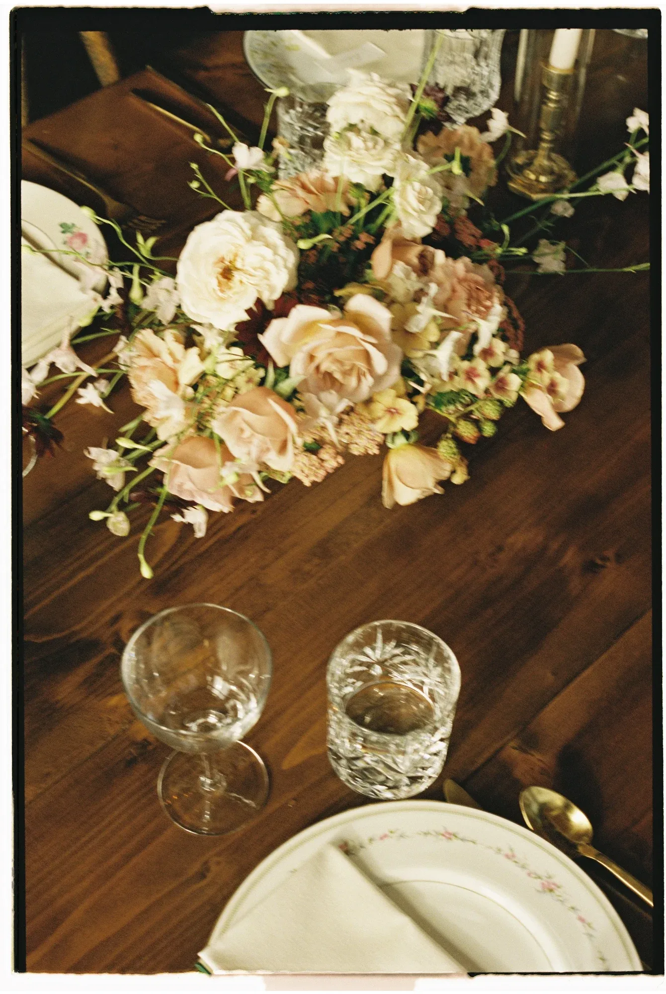 Garden roses and sweet peas trailing across a dark wood table set with vintage china