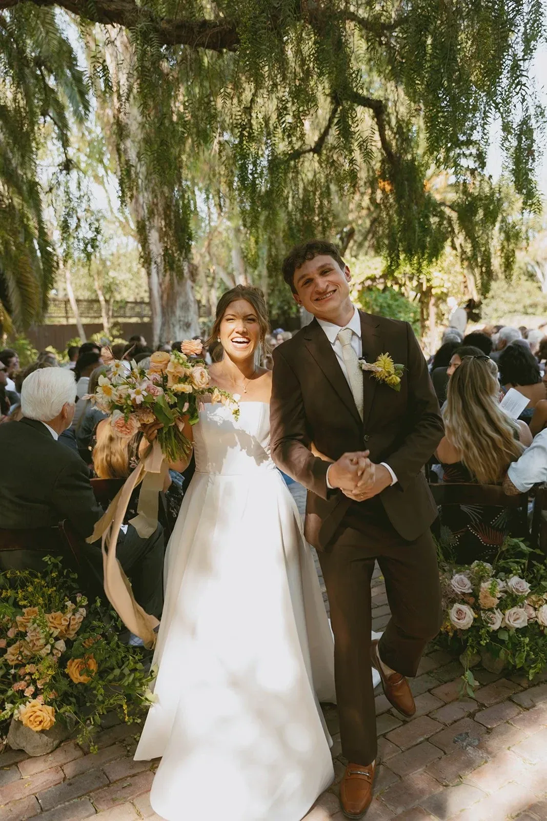A couple walking back down the aisle beneath a willow, guests on either side