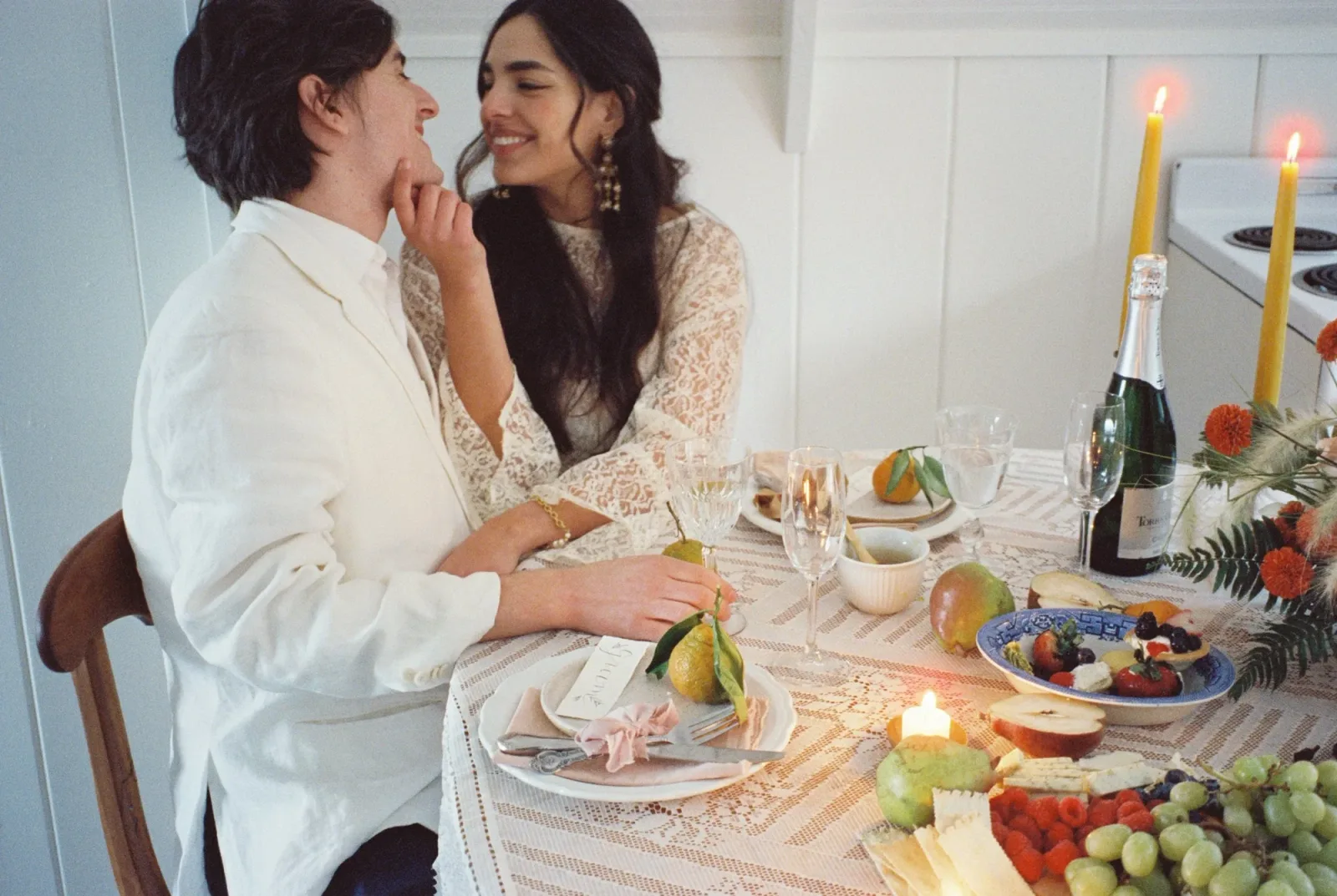 Two people sharing a laugh at a candlelit table of fruit and flowers