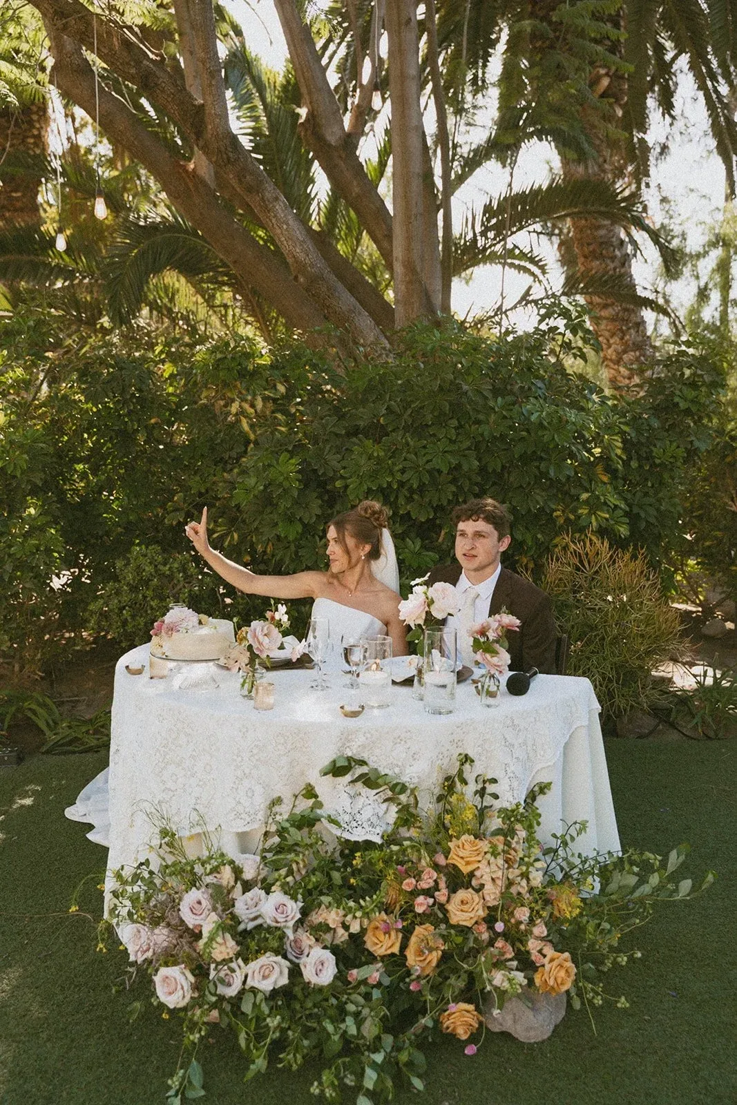 A couple at a sweetheart table in a garden, flowers massed at their feet