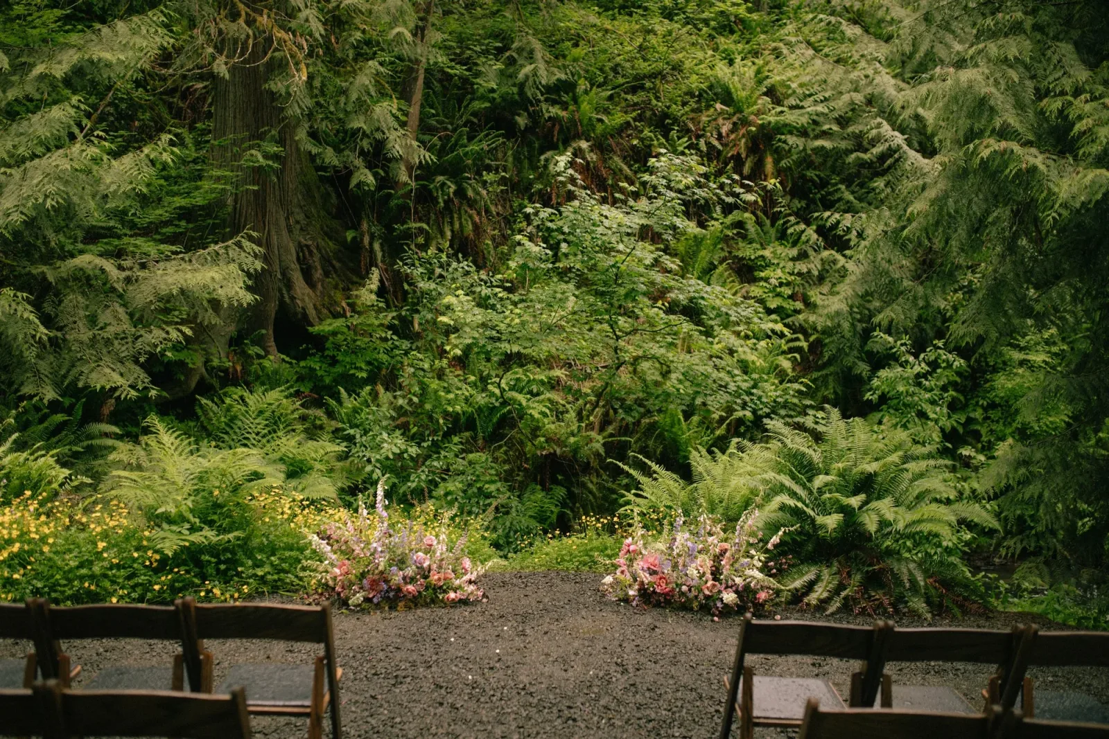 Low floral arrangements marking a ceremony aisle in a fern-filled forest clearing