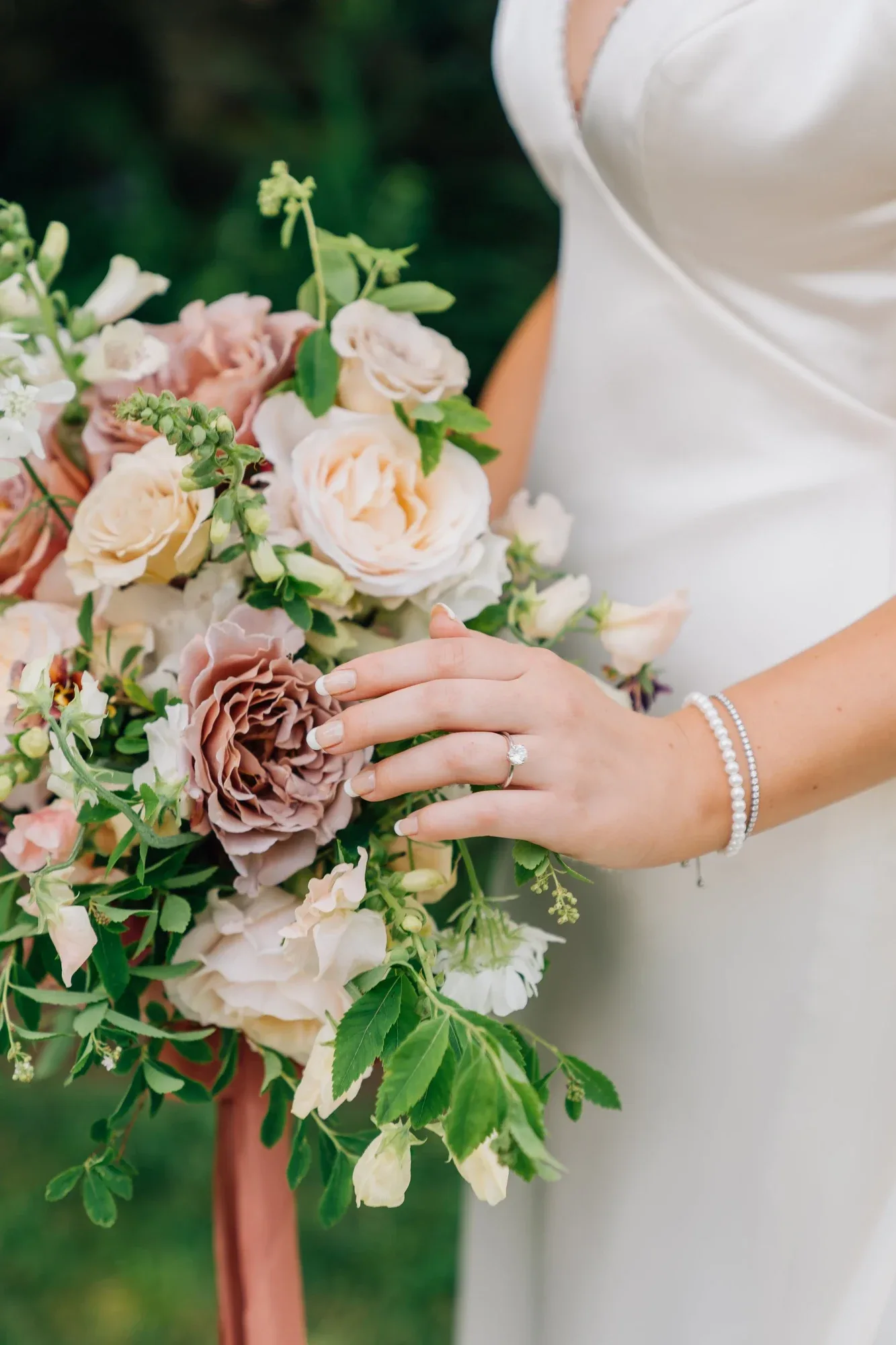 A bride holding a bouquet of mauve and blush roses with a trailing ribbon