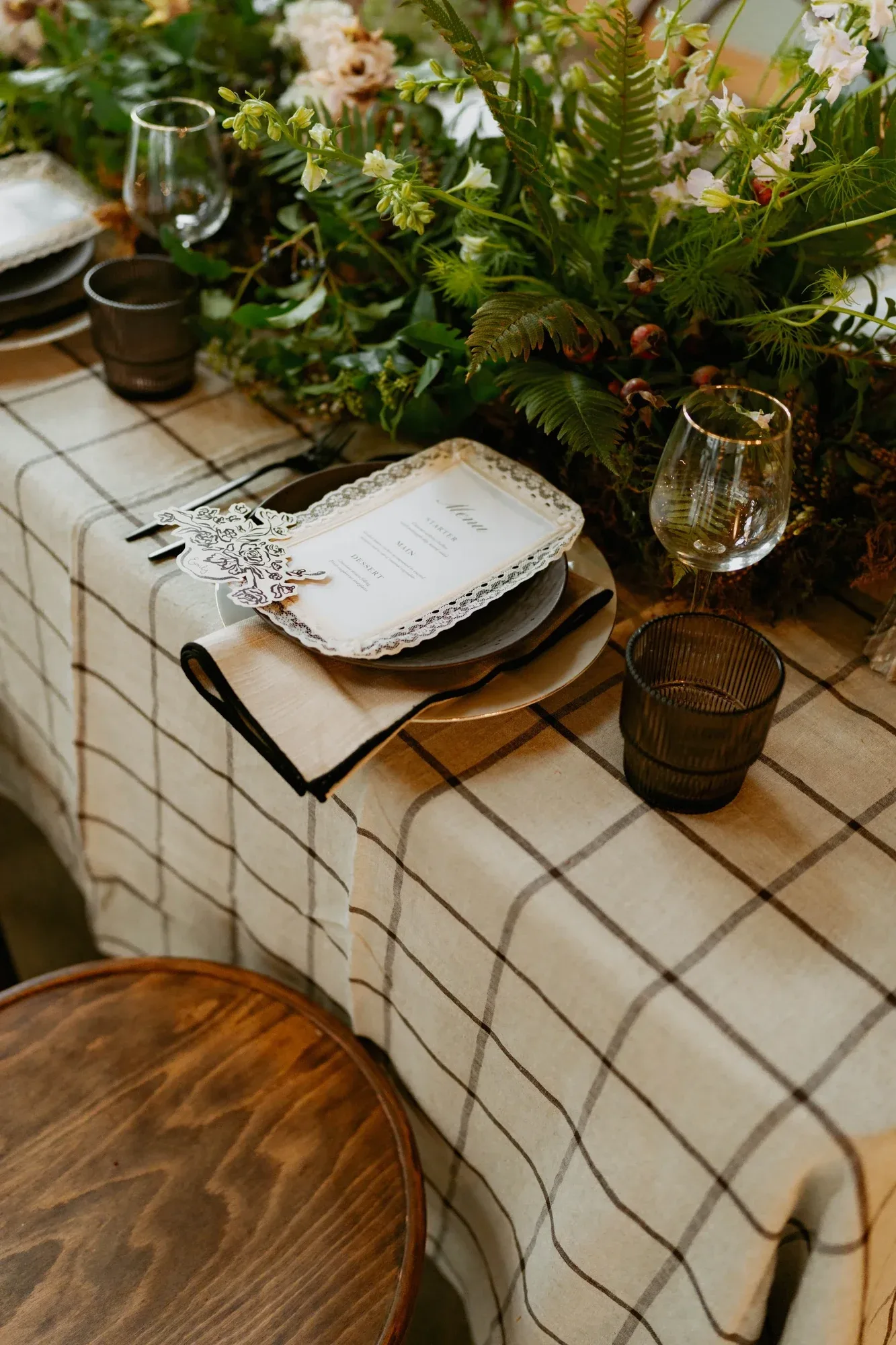 A plaid-linen table set with ferns, garden flowers and a hand-lettered menu